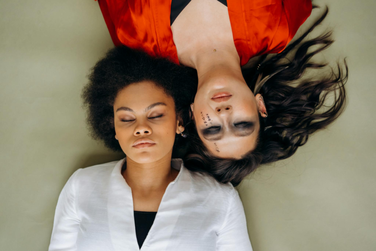 Two women in meditation pose lying head-to-head, embodying peace and spirituality.